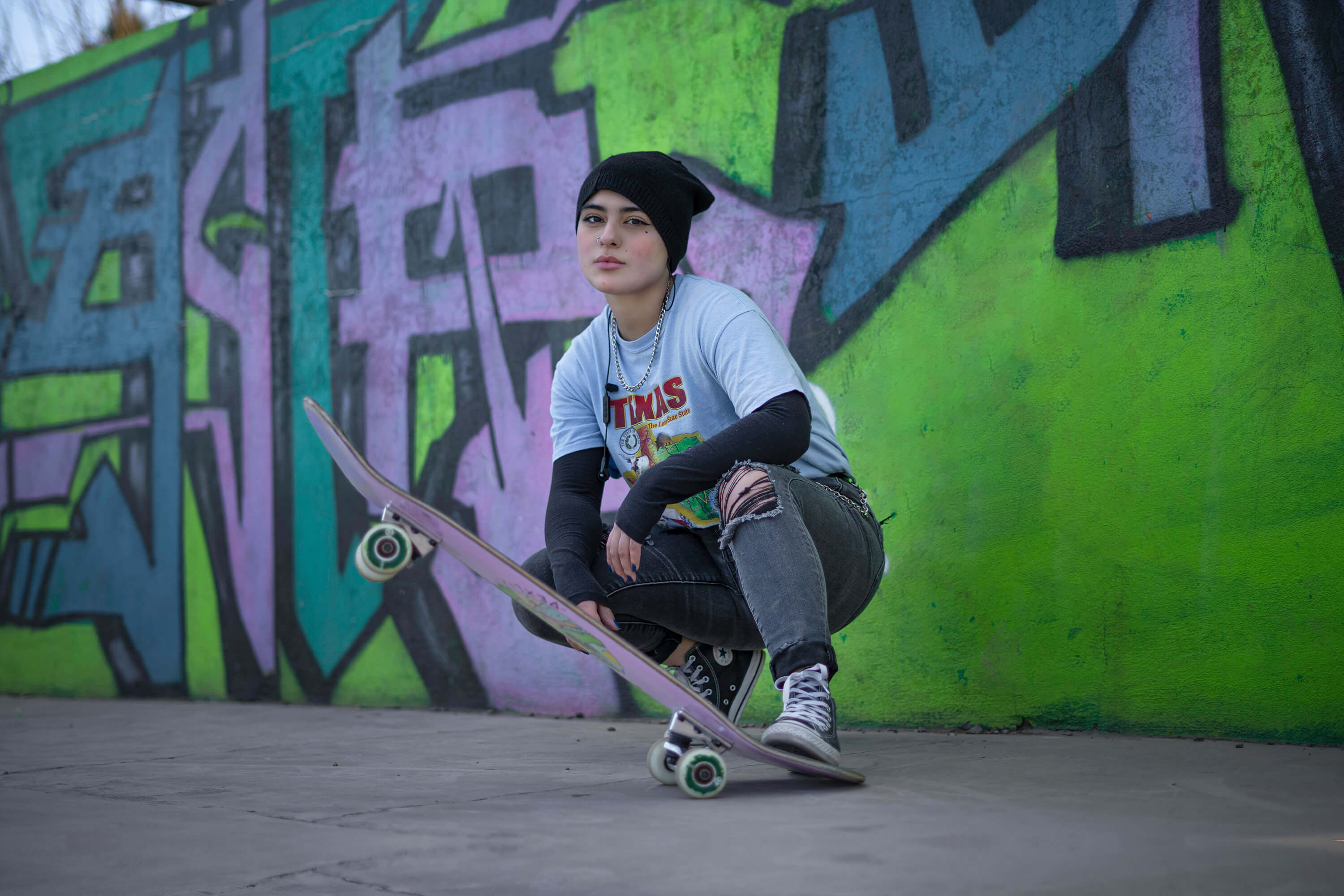 Girl Posing with skateboard in front of graffiti wall. 